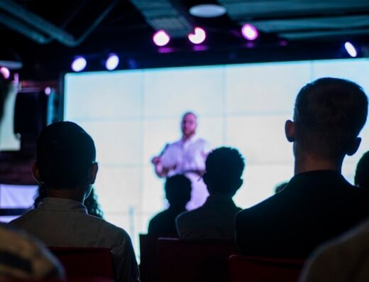 An audience watching a speaker on screen at an event
